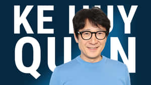 演員關繼威身穿藍色襯衫微笑，身後有他的姓名以大型白色字母呈現。 — 胡桃 壁紙