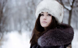 戴著毛帽和外套的女性站在雪林中。 — 冬日美學 壁紙