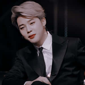 穿著黑色西裝、鉑金髮和紅唇的男士，在鏡頭光暈中擺姿勢。 — Jimin GIF 壁紙