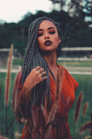 灰色辮子和橙色連衣裙的女性在黃昏時站在高高的草叢中。 — 肖像 壁紙