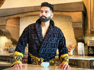 穿著 Versace 長袍的男人靠在廚房櫃檯上，手拿咖啡杯。 — 說唱歌手 壁紙