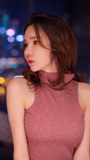 穿著粉紅色高領毛衣的女性，在夜晚閃爍的城市燈光下看向別處。 — 女孩 壁紙