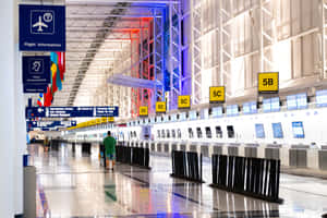 一位旅客穿過現代化的機場客運大樓，設有辦理登機手續櫃檯和航班資訊顯示牌。 — MacBook Air M2 壁紙