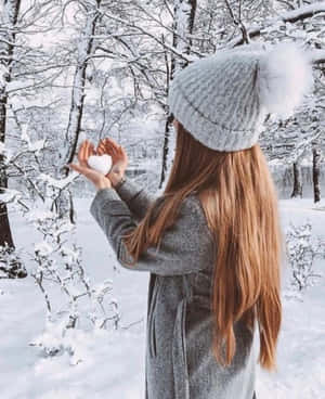 身穿冬季外套的女性在雪地森林中手持心形雪球。 — 冬日美學 壁紙