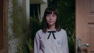 一位身穿校服的年輕女孩在夜間站在門口，溫柔地微笑。 — Netflix GIF 壁紙