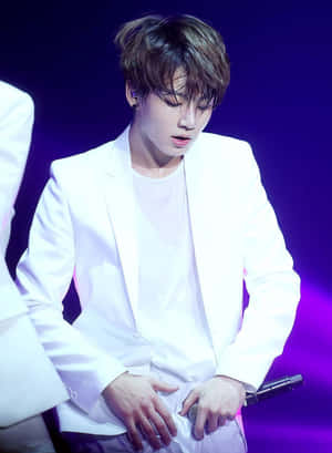 身穿白色西裝的男性K-pop表演者在紫色燈光下的舞台上拿著麥克風。 — Kindle Paperwhite 壁紙