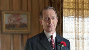 身穿細條紋西裝、佩戴紅色康乃馨的男子，在木鑲板房間。
