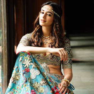 穿著傳統印度長裙（Lehenga）並佩戴金飾的女性在木門旁擺姿勢。 — 日本龍動畫 壁紙