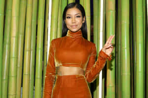 身穿橙色天鵝絨服裝的女性在竹子前比出和平手勢。 — 場地圭介 壁紙