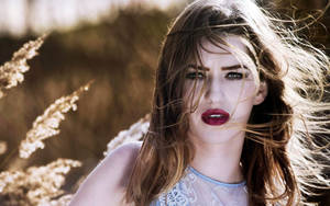 頭髮隨風飄揚、嘴唇鮮紅的女性，在金色田野中，夕陽下。 — 女孩 壁紙