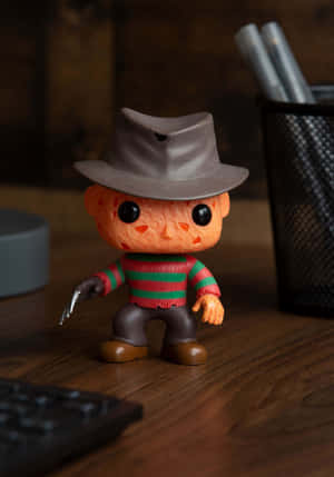 Freddy Krueger Funko Pop 人偶在木桌上，附鍵盤和筆筒。 — Realme Pad 3 壁紙