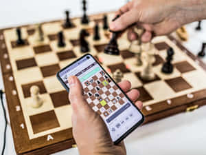 手在實體棋盤和智能手機應用程式上下棋。 — 國際象棋 壁紙