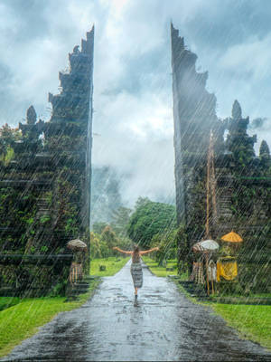 一個人在雨中張開雙臂走過古老的石門。 — 雨天 壁紙