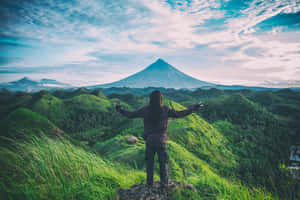 一個人站在山丘上，雙臂大開，面向日出時的山脈。 — 美景 壁紙