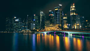 夜晚的城市天際線，有發光的摩天大樓和水面上點亮的橋樑。 — 夜景城市 壁紙