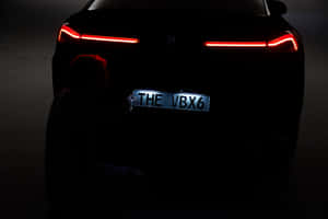 人物在黑暗中跪在帶有發光紅色尾燈的汽車前。 — MacBook 壁紙