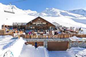 白雪覆蓋的滑雪小屋，人們在戶外座位和纜車旁享受，背景是白雪覆蓋的山脈。 — MacBook Pro M3 壁紙