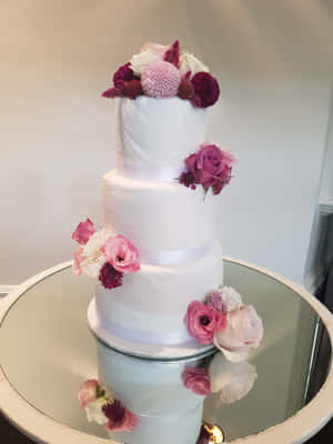 四層白色結婚蛋糕，以粉紅色和酒紅色花朵裝飾，置於鏡面桌上。 — iPad 第9代 壁紙