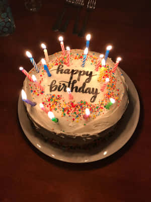 生日蛋糕，有燃點嘅蠟燭同糖針，放喺木枱上。 — 2048x2732 壁紙
