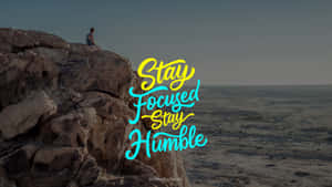 人坐在懸崖邊緣俯瞰沙漠，帶有「Stay Focused Stay Humble」文字。 — 暗黑生活 GIF 壁紙