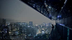 一個人晚上獨自坐在玻璃屋頂上，俯瞰城市。 — 夜景城市 壁紙
