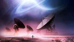 一個人在沙漠中，與巨大的衛星天線一起站在環狀行星下。 — 行星 壁紙