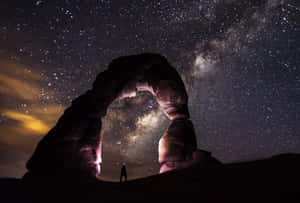 人站在巨大的岩石拱門下，夜晚觀看銀河。 — 可愛星系 壁紙