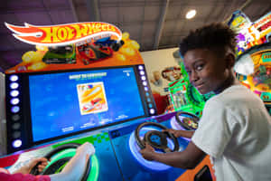 小孩用方向盤玩Hot Wheels街機賽車遊戲。 — 街機 壁紙