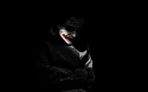 一個帶有塗白臉龐和紅唇的威脅性人物從黑暗中凝視。 — 小丑 壁紙