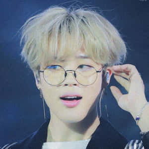 戴眼鏡的年輕表演者在藍色燈光下的舞台上調整耳機。 — Jimin GIF 壁紙
