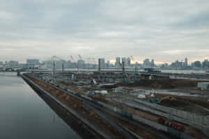 沿河的城市建築工地，背景有起重機和城市天際線。 — MacBook Pro 壁紙