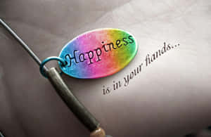 一個刻有「Happiness」的彩虹色飾物放在一隻手上，附近寫著「is in your hands...」。 — 可愛情侶 GIF 壁紙