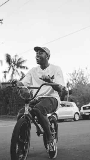 一個年輕男子在棕櫚樹的街道上踩著BMX單車微笑。 — Tyler the creator GIF 壁紙