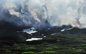 火山噴出濃煙，下方有雪斑和綠色植被。 — 天際線 壁紙
