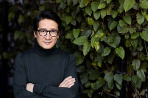 穿黑色高領毛衣和戴眼鏡的男人交叉雙臂靠在常春藤牆上。 — 胡桃 壁紙