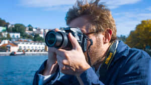 男人在海濱小鎮附近用 Nikon 相機拍照。 — 攝影師 壁紙