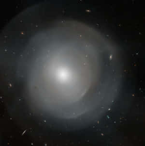 一個明亮的螺旋星系，被深空中遙遠的恆星和星系環繞。 — 1:1 壁紙