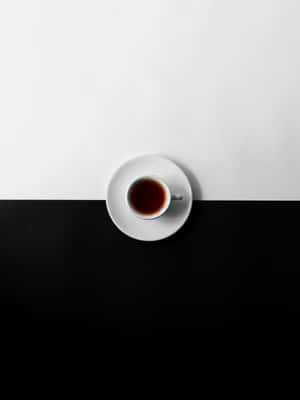 一個白色茶杯裝著深色茶，放在碟子上，位於黑白背景中央。 — HMD Terra M 壁紙