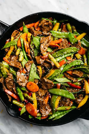 鑄鐵鍋中的炒牛肉和蔬菜，撒上芝麻。 — 2:3 壁紙