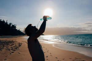 男人喺陽光海灘飲水，有海浪 — 夏日氣息 壁紙