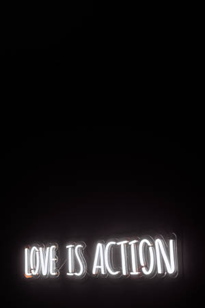 霓虹燈牌在黑色牆壁上以白光顯示 love is action。 — 霓虹美學 壁紙