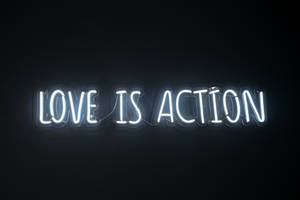 霓虹燈牌在黑色牆上顯示love is action。 — 愛就是愛 壁紙