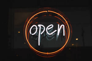 一個發光的霓虹燈牌，在圓形框架內寫著open，置於深色商店櫥窗上。 — 橙色圓圈 壁紙