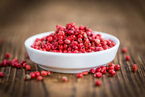 一個白色陶瓷碗裝滿紅色胡椒粒，放在木桌上。 — 淺粉紅色美學動圖 壁紙