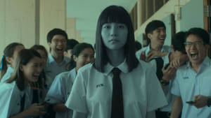 一個穿著校服的安靜女學生平靜地站著，同學們在她周圍大笑。 — Netflix GIF 壁紙
