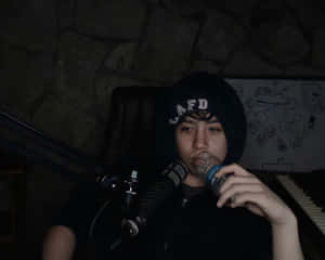 穿著深色連帽衫的人坐在麥克風前從罐中飲用。 — YouTube 壁紙