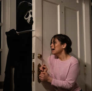 穿粉紅色毛衣的女人被門口持刀的蒙面殺手嚇壞。 — 尖叫 壁紙