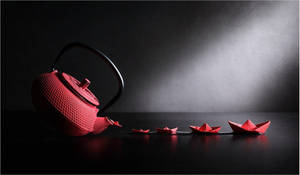 紅色茶壺在聚光燈下將紅色紙船灑落在深色反光表面上。 — 紅色美學 壁紙