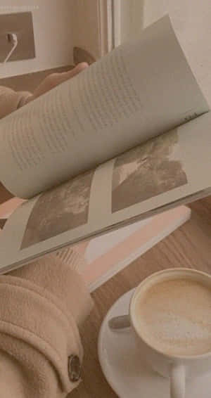 雙手在木桌上的咖啡杯旁閱讀一本書。 — Pixel Fold 壁紙