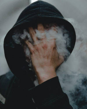 身穿深色連帽衫的人用手遮住臉，白色蒸氣在周圍翻騰。 — 煙霧動畫 壁紙